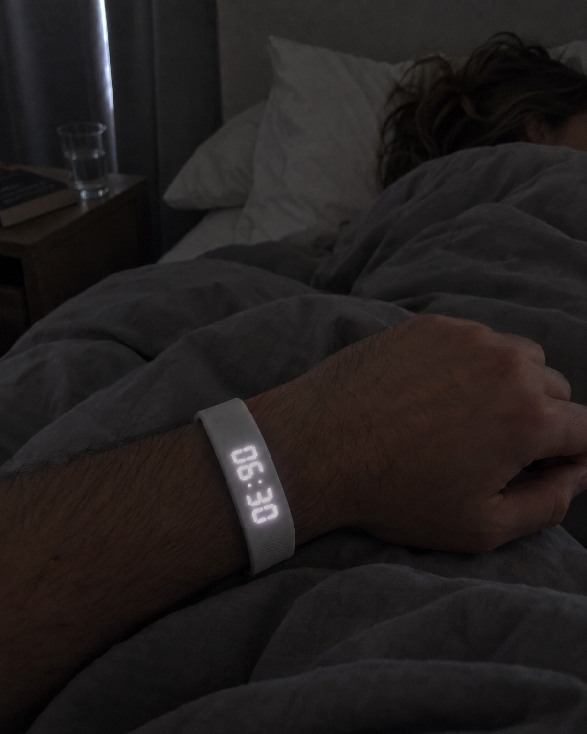 A man sits up in bed at 6:30 wearing Nemi while his partner sleeps beside him