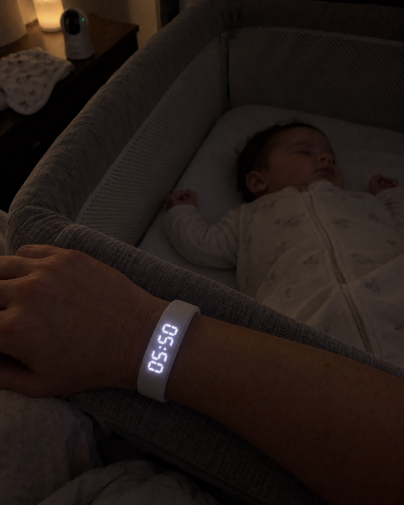 Parent's wrist with the Nemi band on a bassinet while the baby sleeps